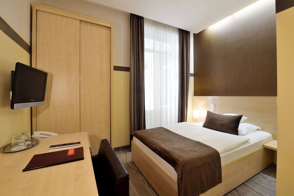 Hotellihuone, jossa on sänky, yöpöytä, televisio, työpöytä ja vaatekaappi.