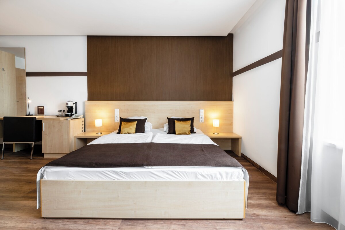A hotel room with a large bed, bedside tables, a desk, and a chair.