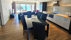 A modern kitchen with a dining area, wooden flooring, and a view of the outdoors. - Sea Spray Suites  (Paihia)