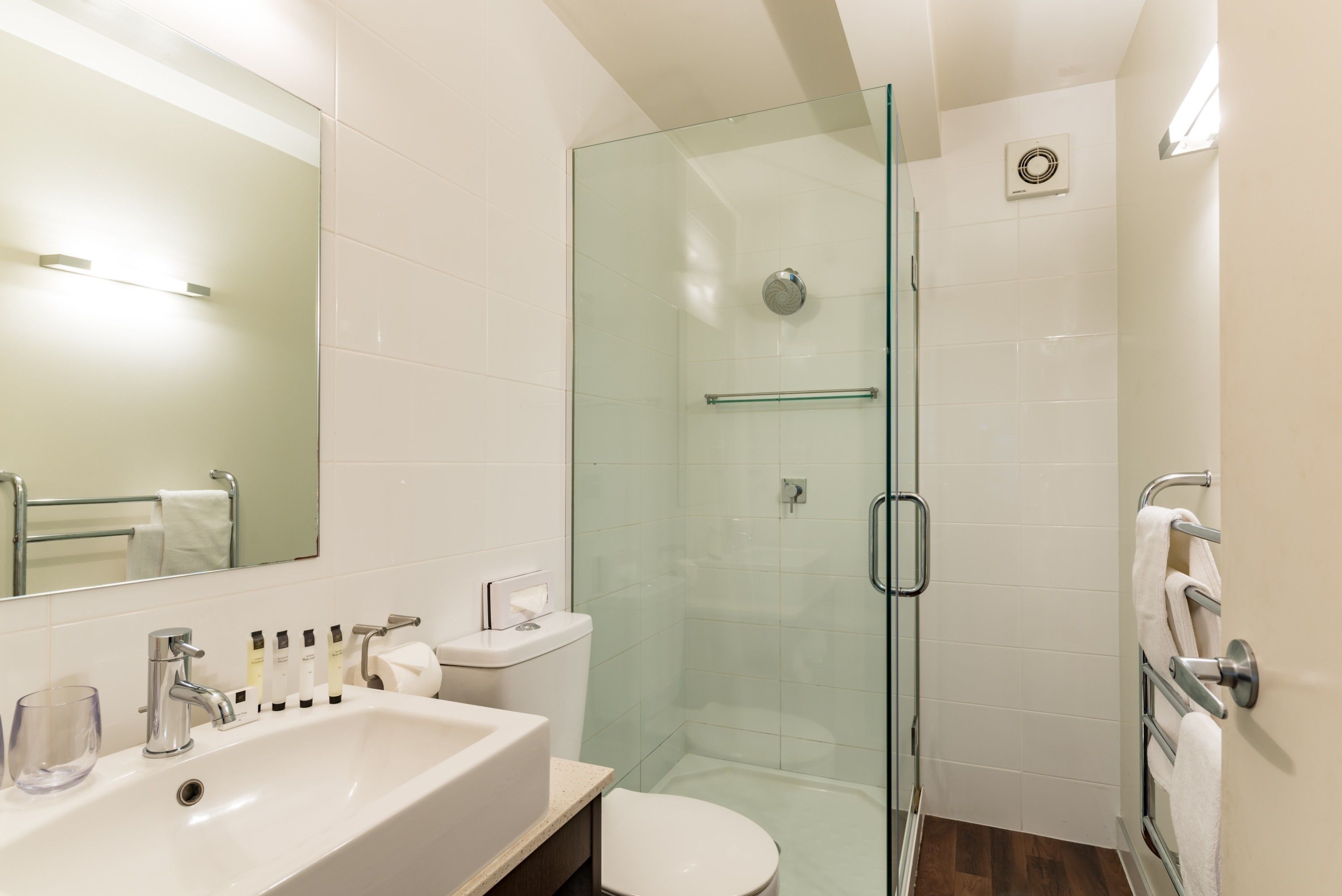 A modern bathroom with a glass-enclosed shower, a white sink with a mirror above, and a toilet.
