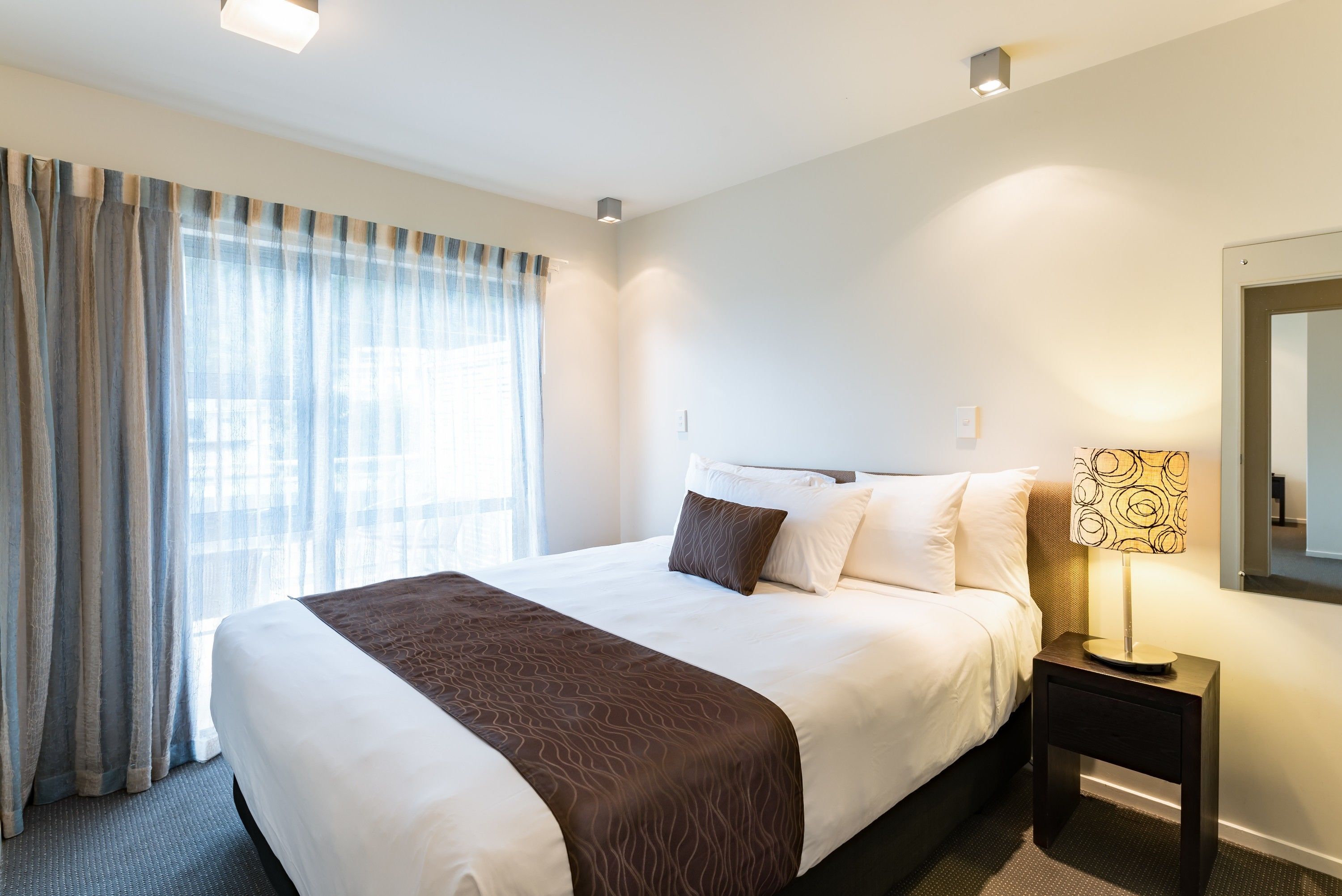 A hotel room with a large bed, a nightstand with a lamp, and a window with curtains.