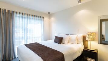 A hotel room with a large bed, a nightstand with a lamp, and a window with curtains.