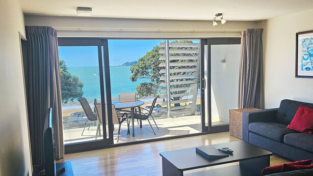 A living room with a sofa, coffee table, and a view of the sea through large glass doors. - Sea Spray Suites  (Paihia)