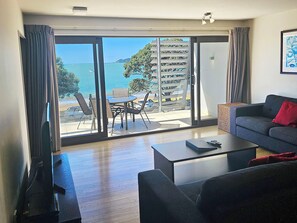 A living room with a sofa, coffee table, and a view of the sea through large glass doors.