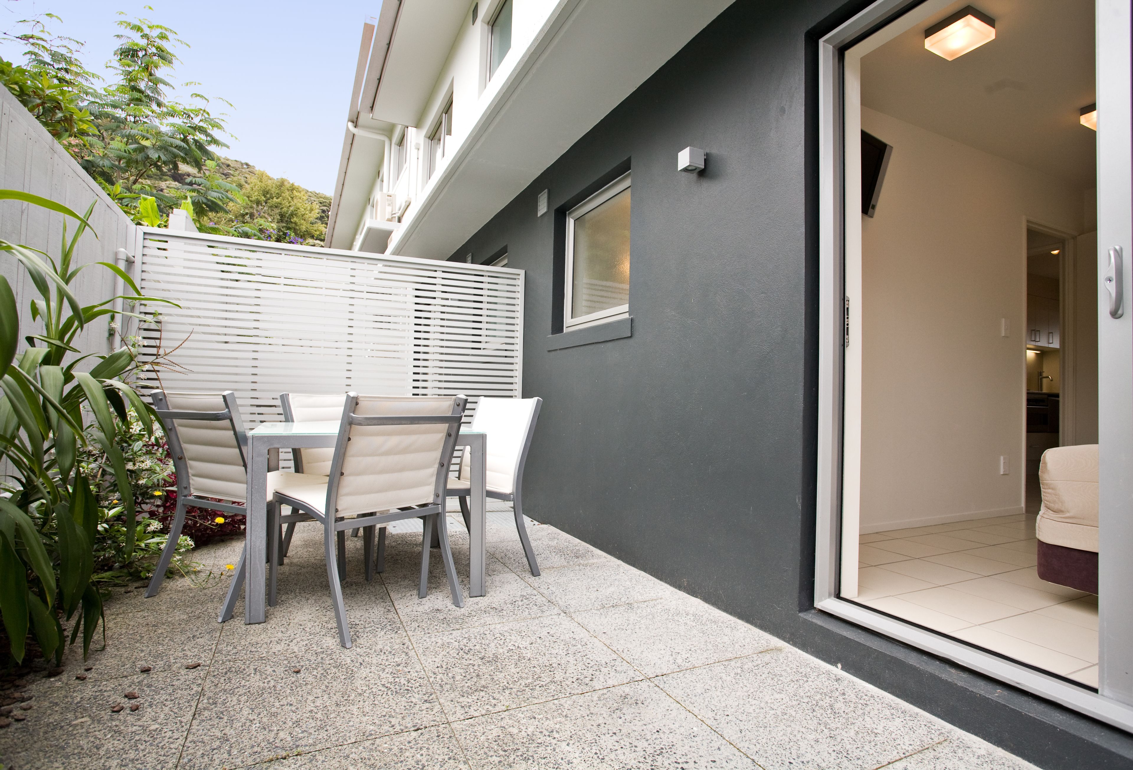 A patio with a table and chairs, a sliding glass door leading to an interior space, and a grey wall.