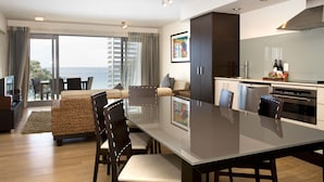 A modern kitchen with a dining area, large windows, and a view of the sea. - Sea Spray Suites  (Paihia)