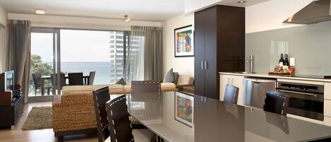 A modern kitchen with a dining area, large windows, and a view of the sea.