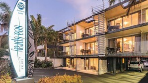 A multi-story hotel with balconies, a parking area, and a sign for Sea Spray Suites. - Sea Spray Suites  (Paihia)