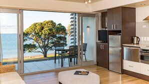 A modern kitchen with a large window, a dining area with chairs, and a view of the sea. - Sea Spray Suites  (Paihia)