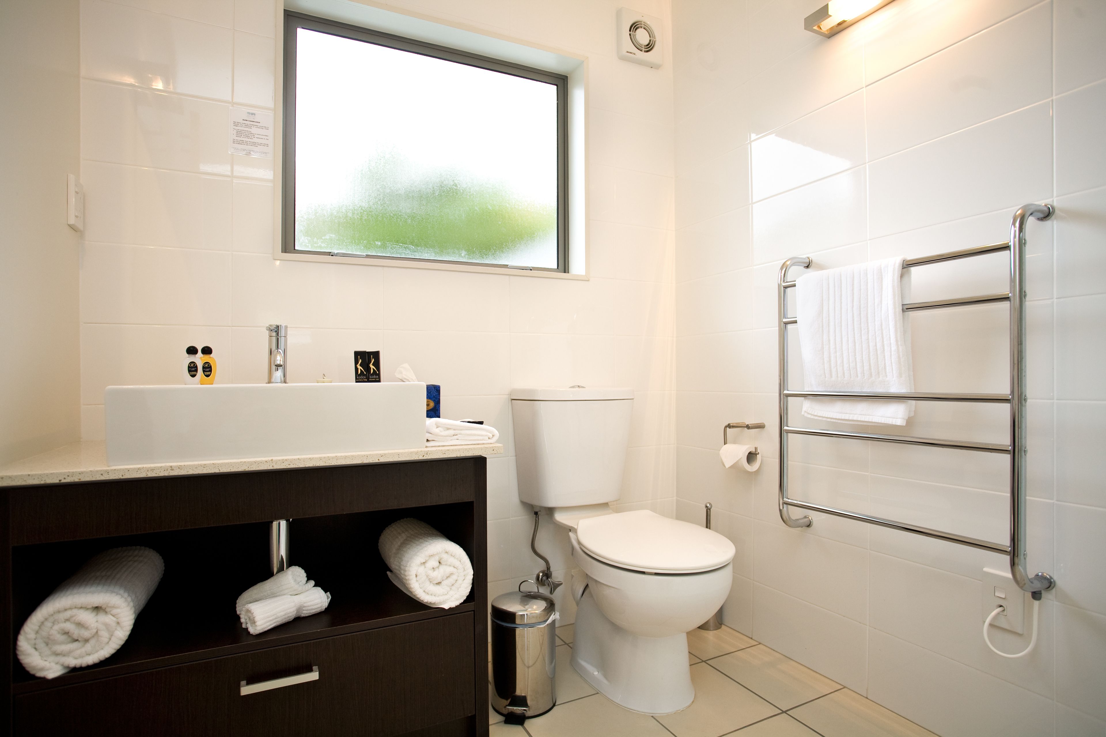 Un baño moderno con inodoro blanco, lavabo con espejo y toallero.