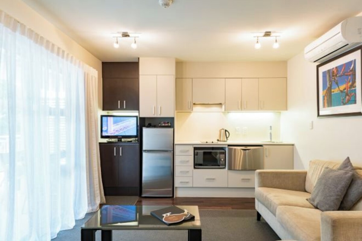 A compact living space with a kitchenette, a flat-screen TV, a sofa, and a coffee table.