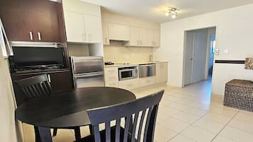 Uma cozinha moderna com uma mesa de jantar e cadeiras, geladeira, fogão, micro-ondas e lava-louças.