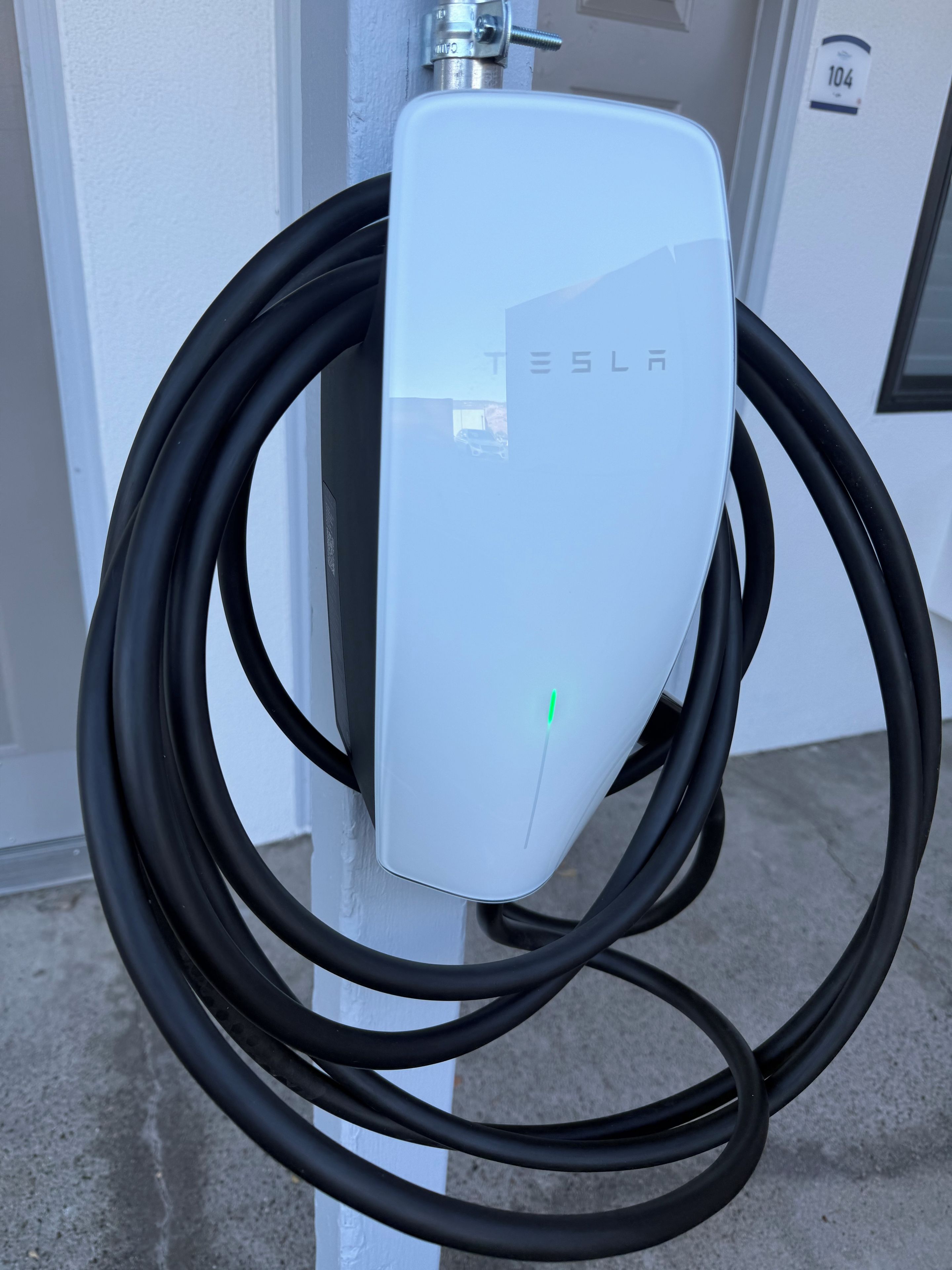 A white Tesla charging station with a visible charging cable.