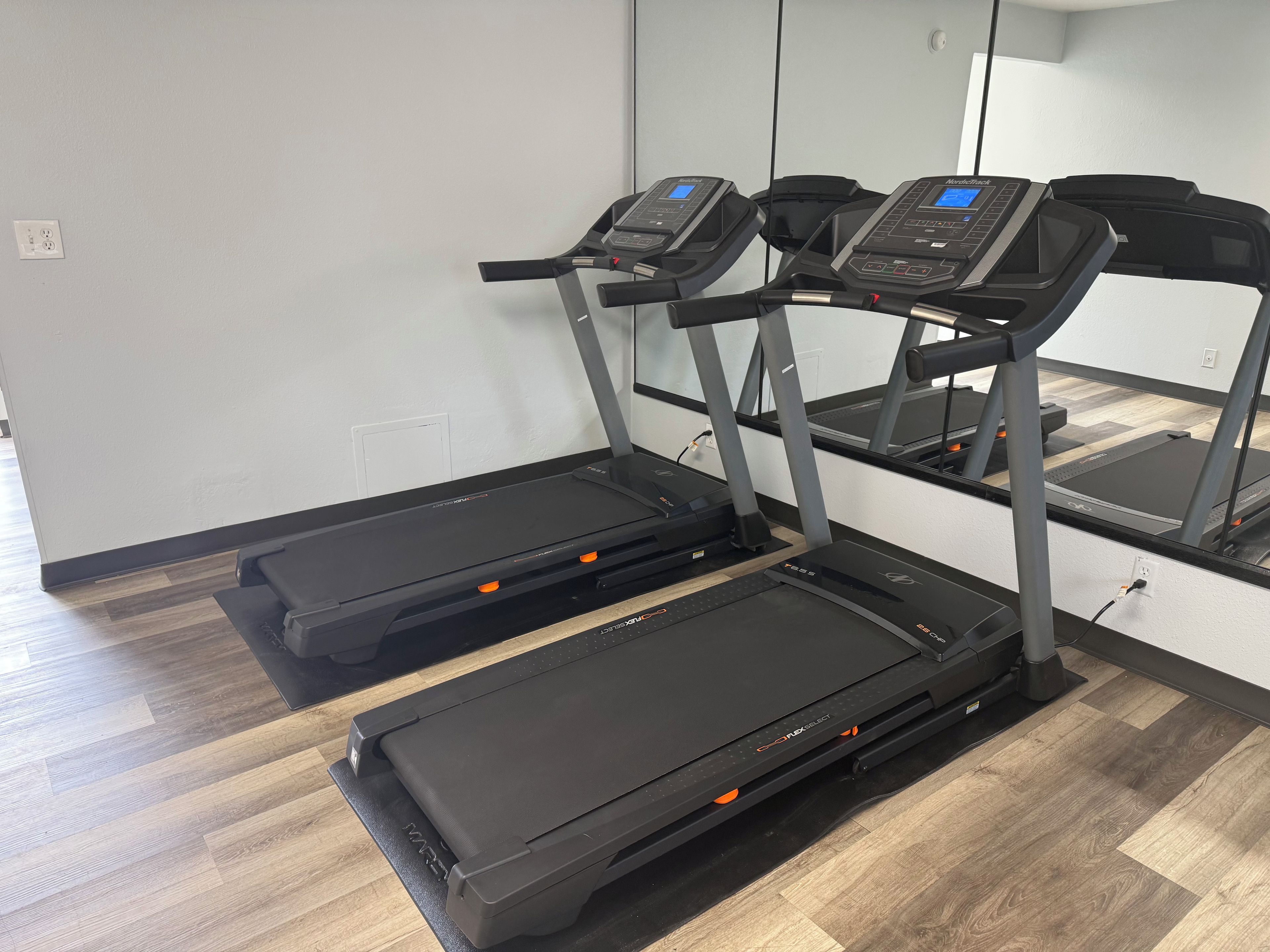 Une pièce équipée de deux tapis de course, d’un miroir et d’un plancher en bois.