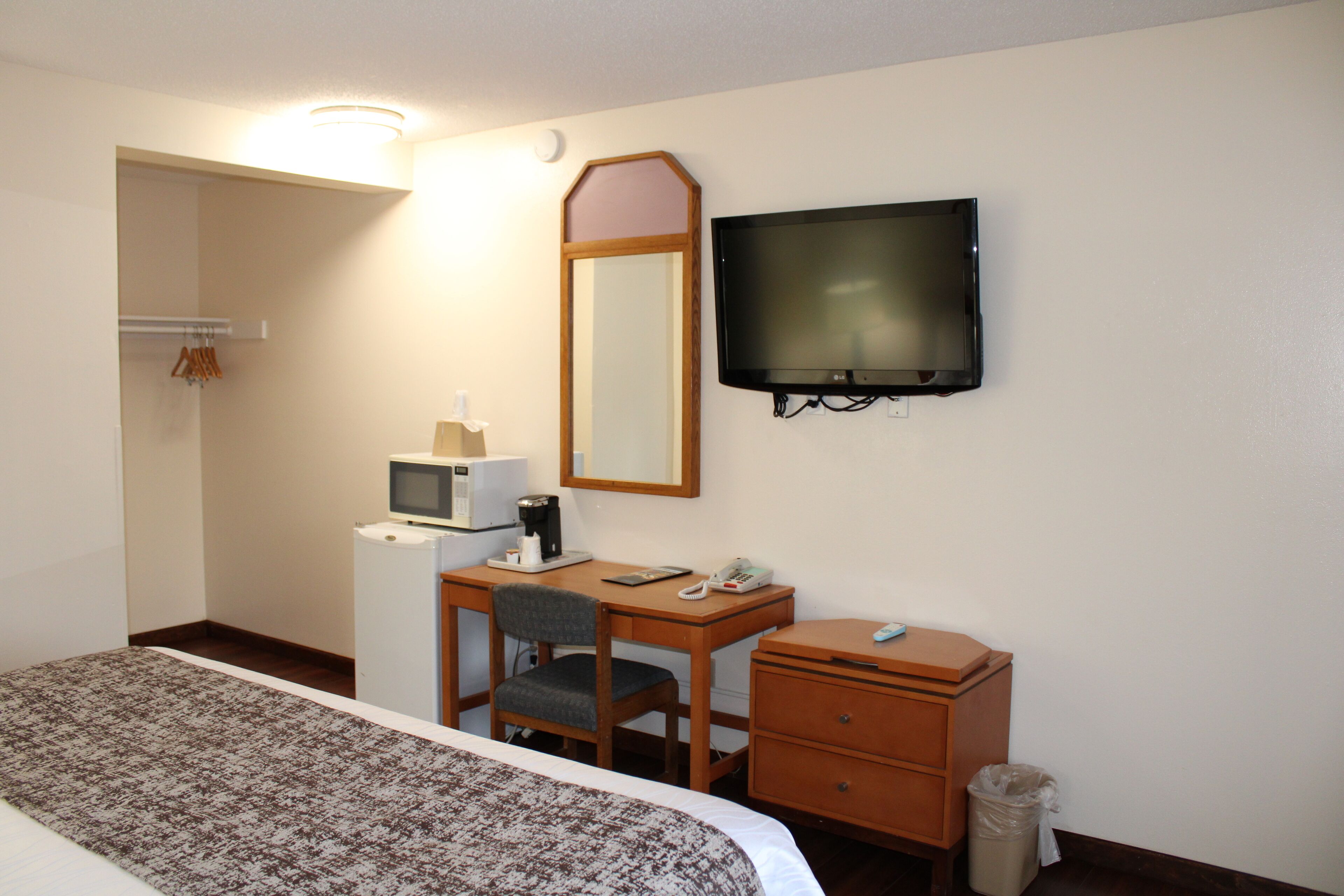 Hotellihuone, jossa on sänky, työpöytä, tuoli, televisio, mikroaaltouuni ja roskakori.