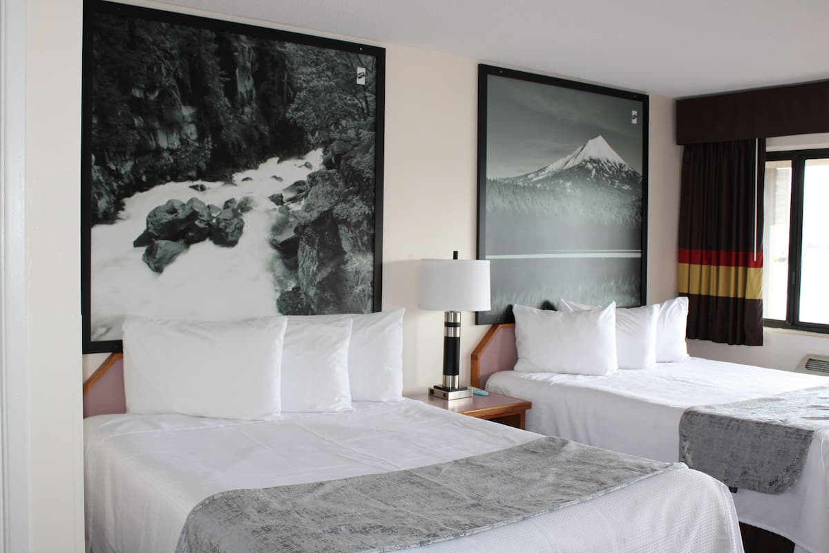 A hotel room with two beds, a large framed picture of a mountain, a lamp, and a window with curtains.