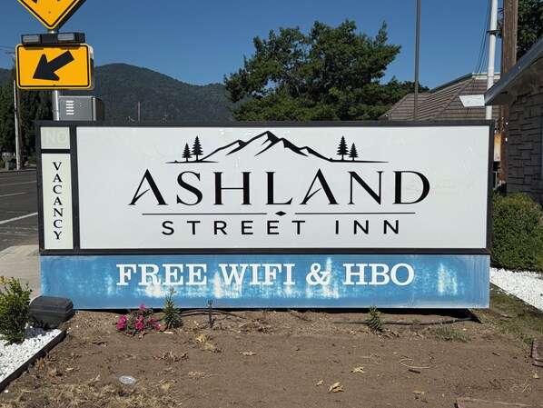 A street sign for Ashland Street Inn with a mountain and trees graphic, a vacancy sign, and a blue sign stating free WiFi & HBO. - Ashland Street Inn (Ashland)