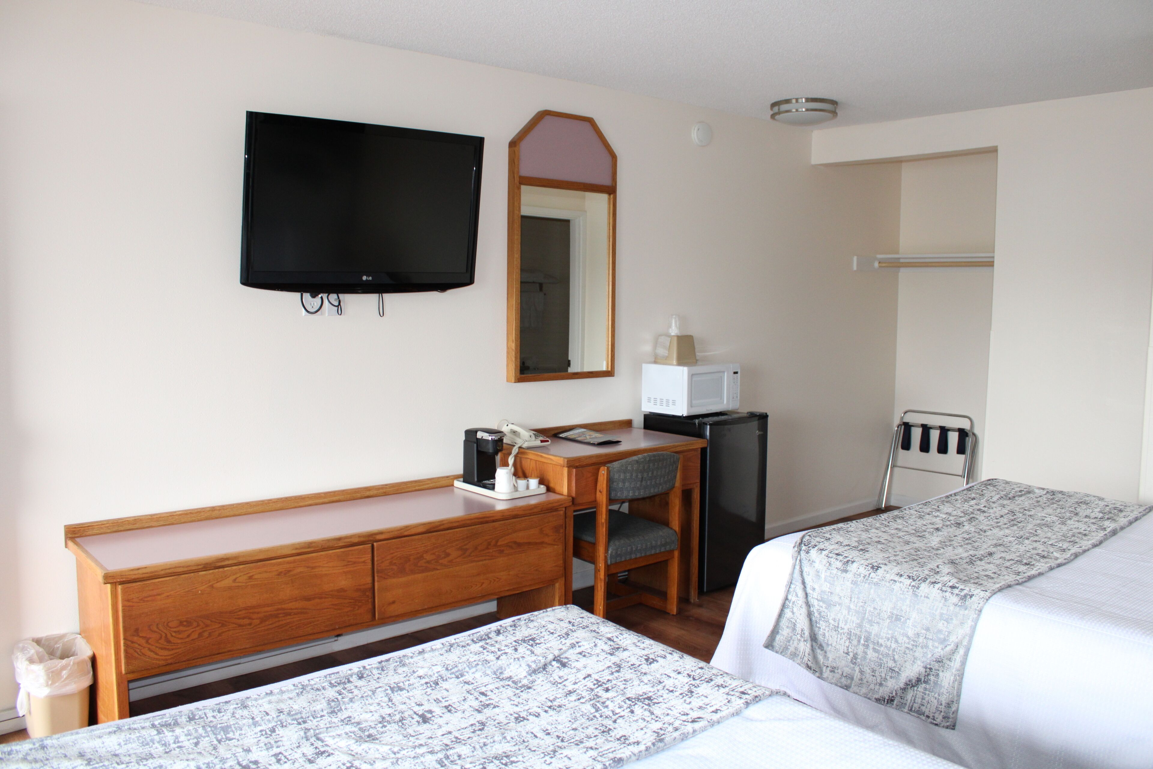 A hotel room with a wooden desk, a television, a microwave, a refrigerator, and two beds with gray bedding.