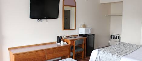 A hotel room with a wooden desk, a television, a microwave, a refrigerator, and two beds with gray bedding.