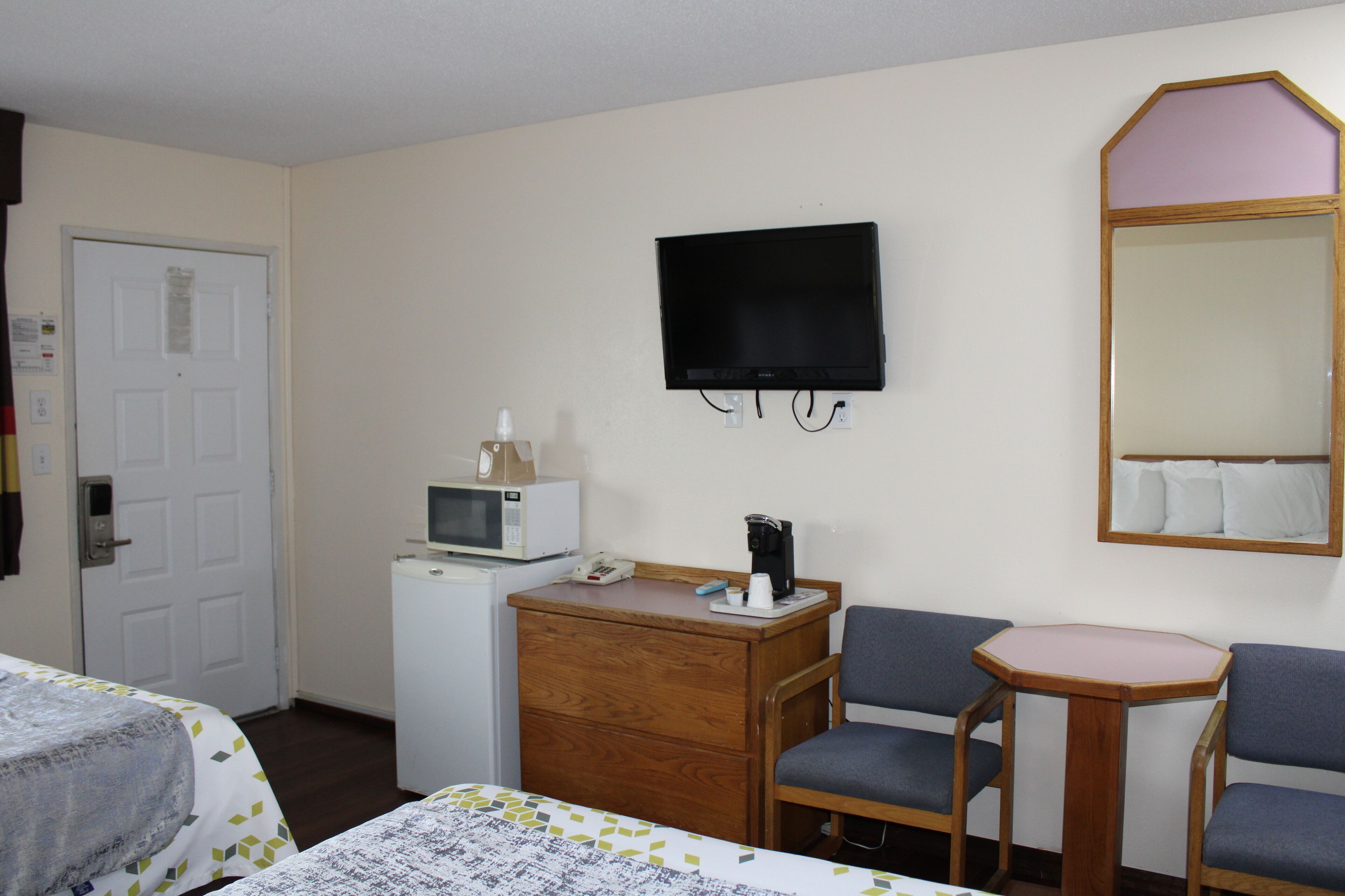 A hotel room with a bed, a desk with a microwave, a television, and a mirror.