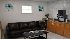 A modern living room with a brown leather sofa, a black coffee table, and a kitchen area with wooden cabinets and a marble backsplash. - Baymont by Wyndham (Ashland)