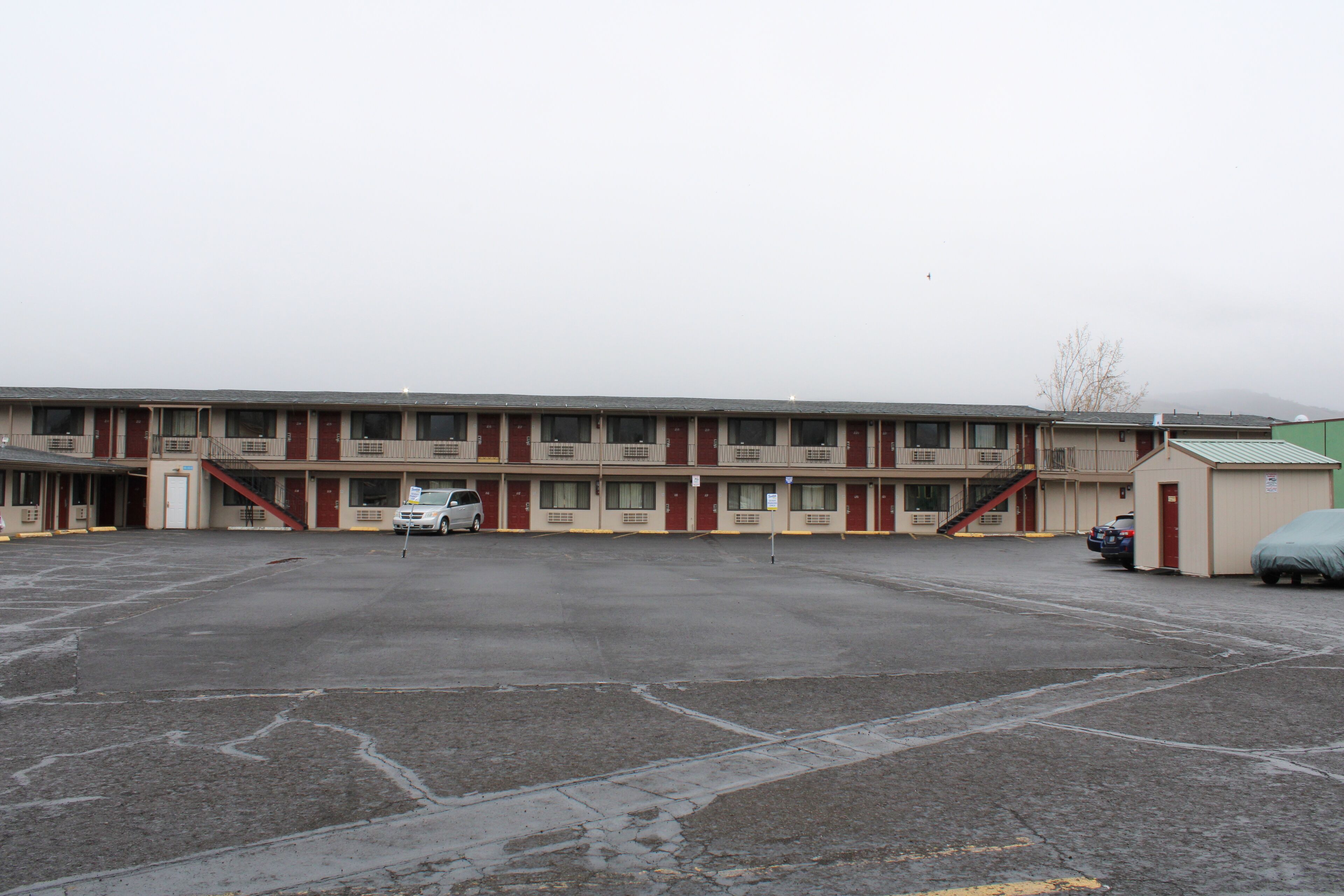 Un motel con un estacionamiento central, varias habitaciones y un pequeño edificio contiguo.