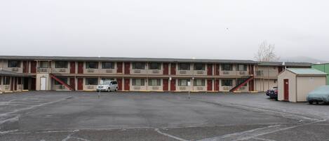 Un motel con un estacionamiento central, varias habitaciones y un pequeño edificio contiguo.