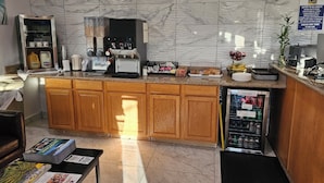 A hotel kitchen with marble tiles, a coffee machine, a refrigerator, and a counter with various items. - Baymont by Wyndham (Ashland)
