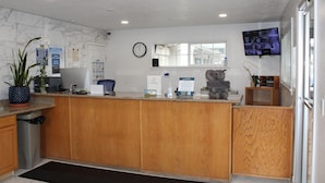 A reception area with a wooden counter, a clock, a television, and a window with blinds. - Baymont by Wyndham (Ashland)