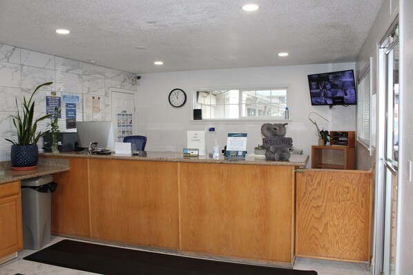A reception area with a wooden counter, a clock, a television, and a window with blinds. - Baymont by Wyndham (Ashland)