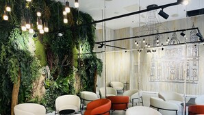 Un interior moderno con una pared verde, sillas blancas y anaranjadas, y un mural de un edificio.