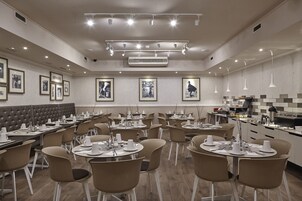 A modern dining area with multiple tables and chairs, a central buffet station, and framed pictures on the walls.