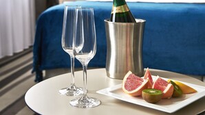 Habitación de hotel con una cama, una mesita de noche con una botella de champán, dos copas y un plato de fruta.