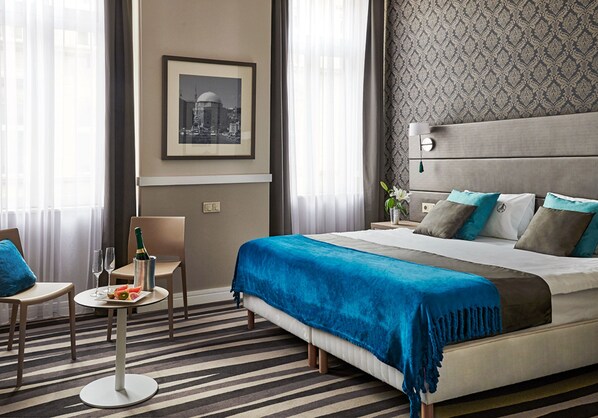 A hotel room with a bed, a small table with a bottle and glasses, a chair, and a framed picture on the wall. - Hotel Central Basilica (Budapest)