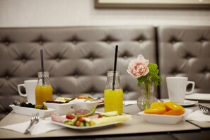 A dining table set with breakfast items, including fruits, vegetables, and beverages, in a room with a tufted sofa. - Hotel Central Basilica (Budapest)