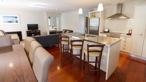A modern kitchen with a central island, bar stools, and a dining area with a wooden table and sofas. - Russell Cottages Tanoa Hotels (Russell)