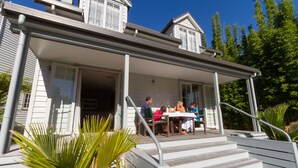 A house with a covered porch, a staircase, and a dining area with people. - Russell Cottages Tanoa Hotels (Russell)