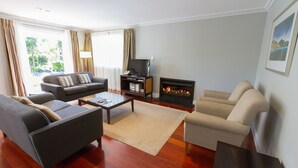 A living room with a sofa, armchairs, a coffee table, a fireplace, and a television. - Russell Cottages Tanoa Hotels (Russell)