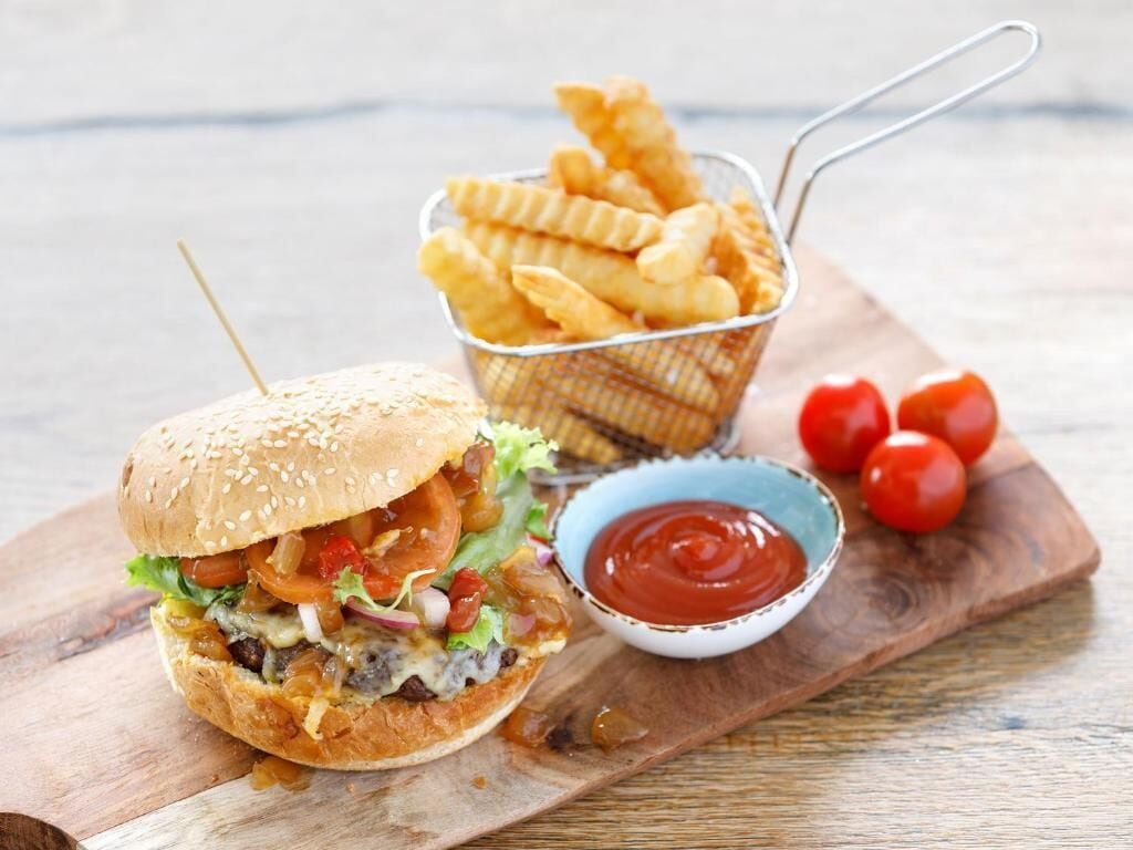 Un hamburger accompagné de frites et de ketchup, servi sur une planche en bois.