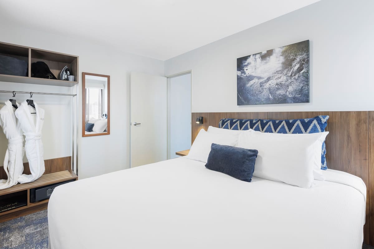 A hotel room with a bed, a wardrobe, a mirror, and a painting on the wall.