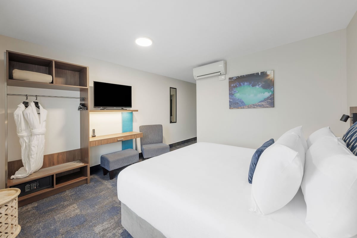 A modern hotel room with a large bed, a seating area, a wardrobe, a flat-screen TV, and an air conditioning unit.