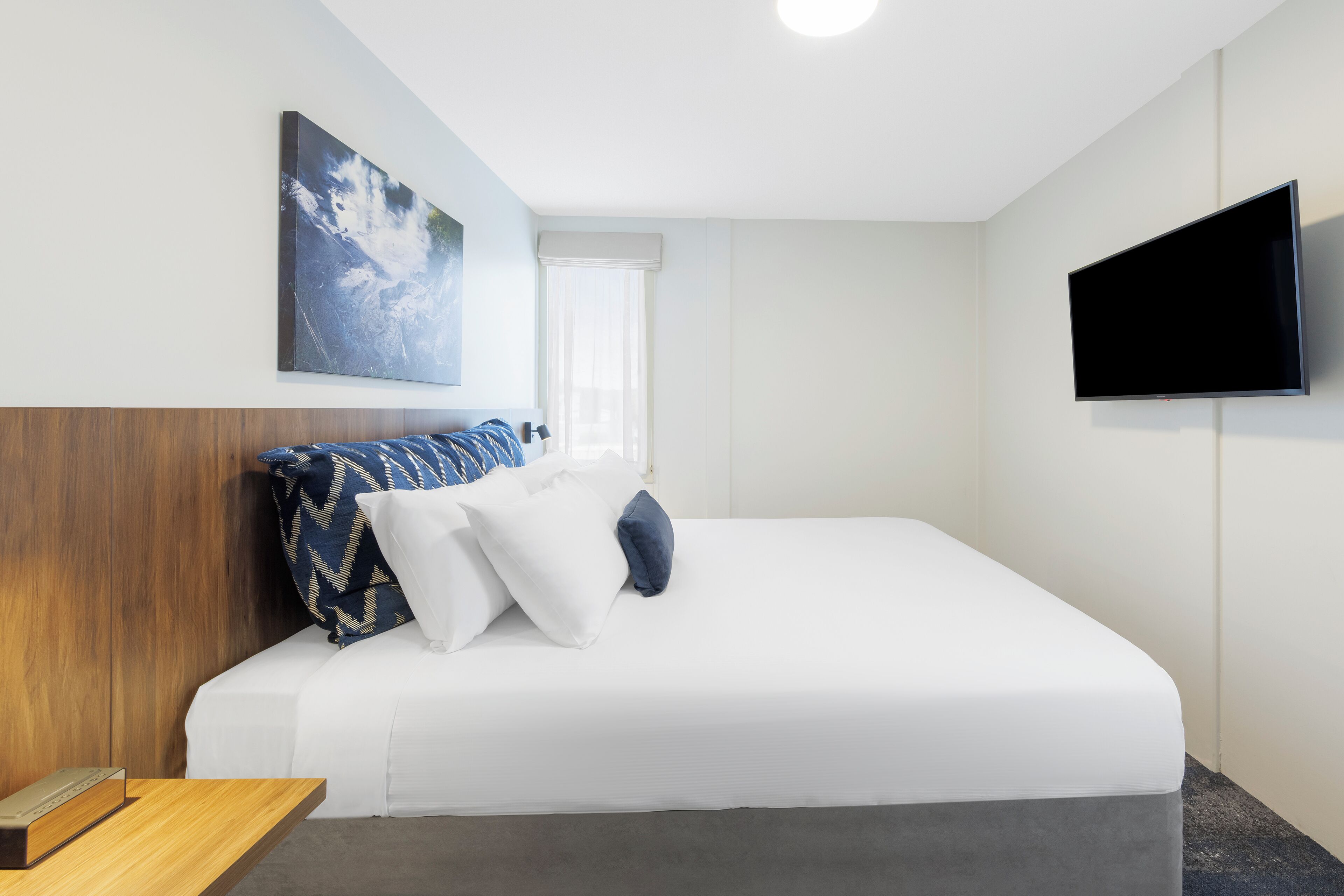 A hotel room with a bed, a flat-screen TV, and a painting on the wall.