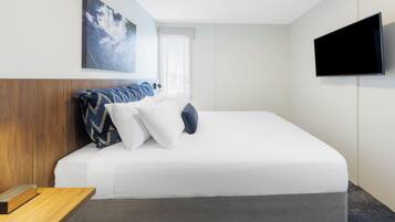 A hotel room with a bed, a flat-screen TV, and a painting on the wall.