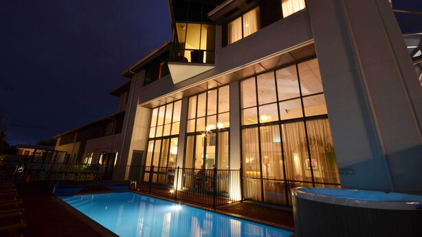 A modern hotel with a swimming pool, large windows, and a well-lit exterior at night. - JetPark Hotel Rotorua (Rotorua)