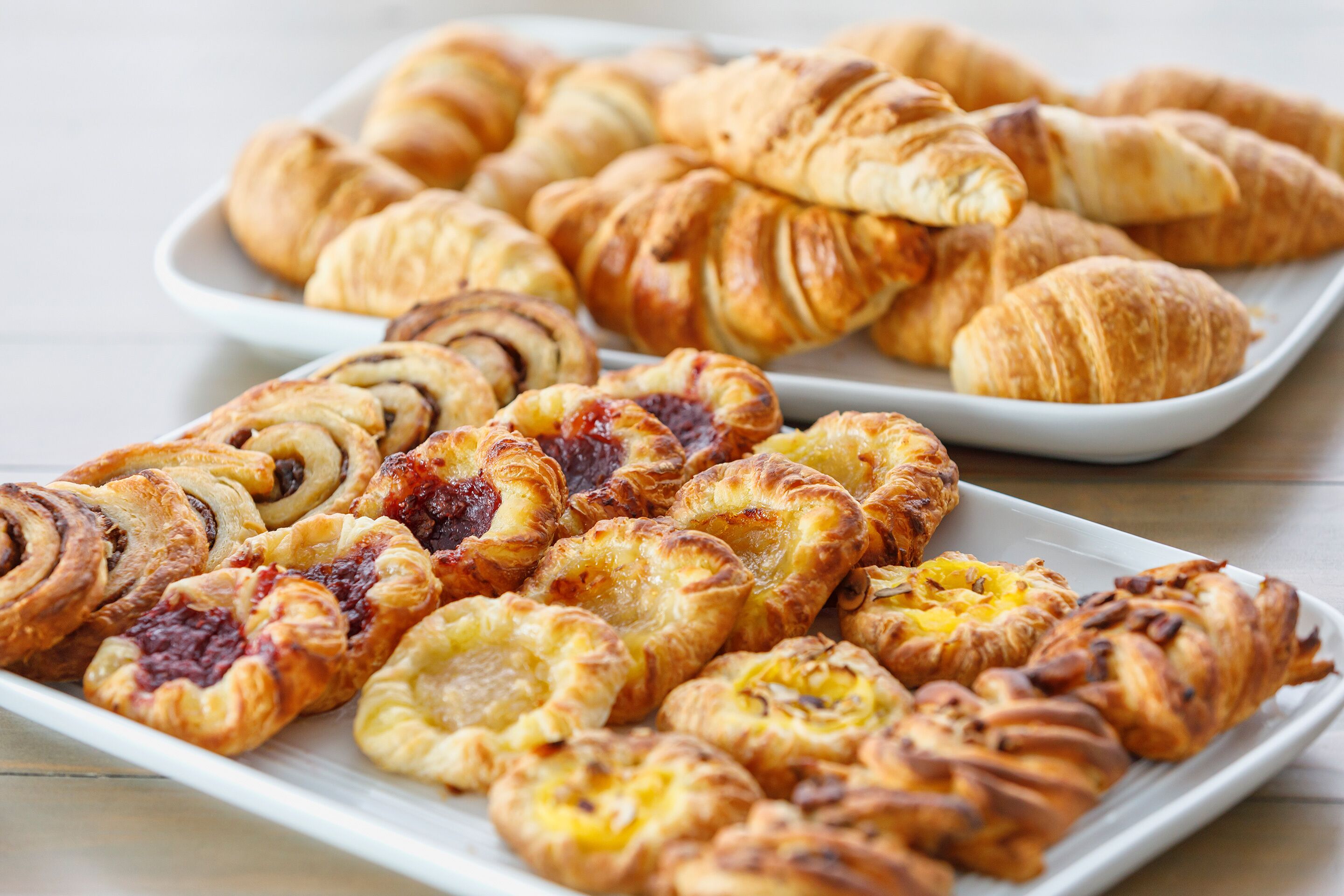 Diversos doces numa placa branca, incluindo croissants e pasteis recheados.