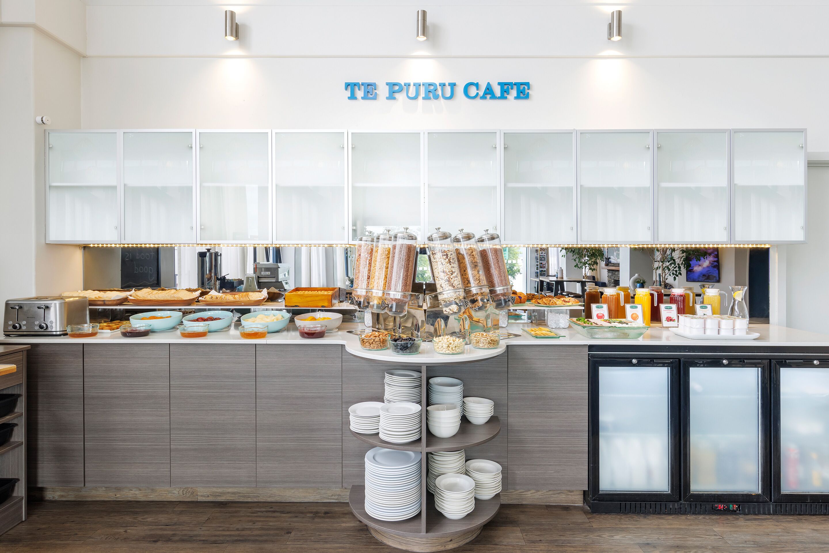 Montaje tipo bufé con diversos alimentos y bebidas, una máquina de café y un letrero que dice "TE PURU CAFE".