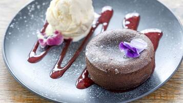 Un plato de postre con pastel de chocolate y una bola de helado de vainilla, decorado con una flor morada y bañado en salsa roja.