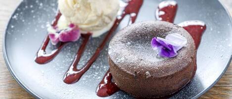 A dessert plate with a chocolate cake and a scoop of vanilla ice cream, garnished with a purple flower and drizzled with red sauce.