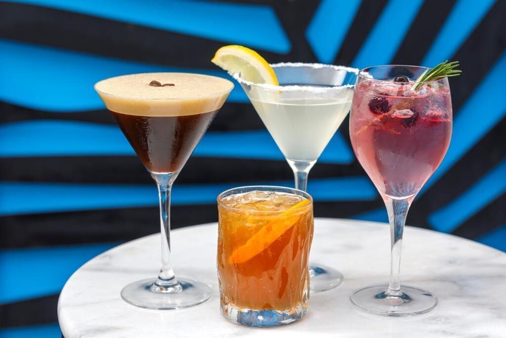 Four different drinks in various glassware against a blue and black striped background.
