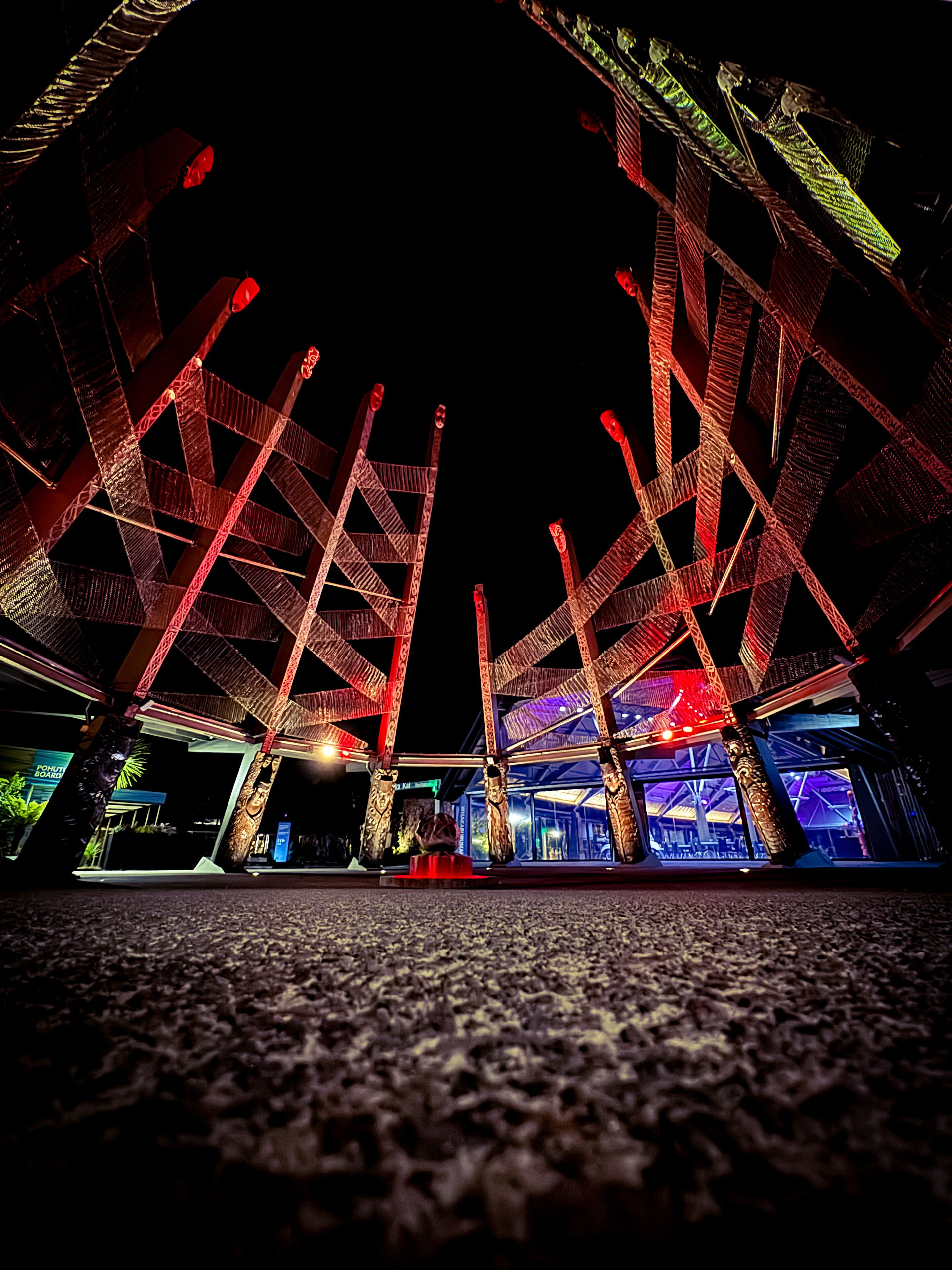 A nighttime view of a building with a unique, illuminated structure featuring geometric patterns and red lighting.